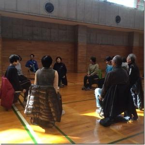 体育館の中で、10名程が椅子に座って輪になりストレッチの講習を受けている様子の写真